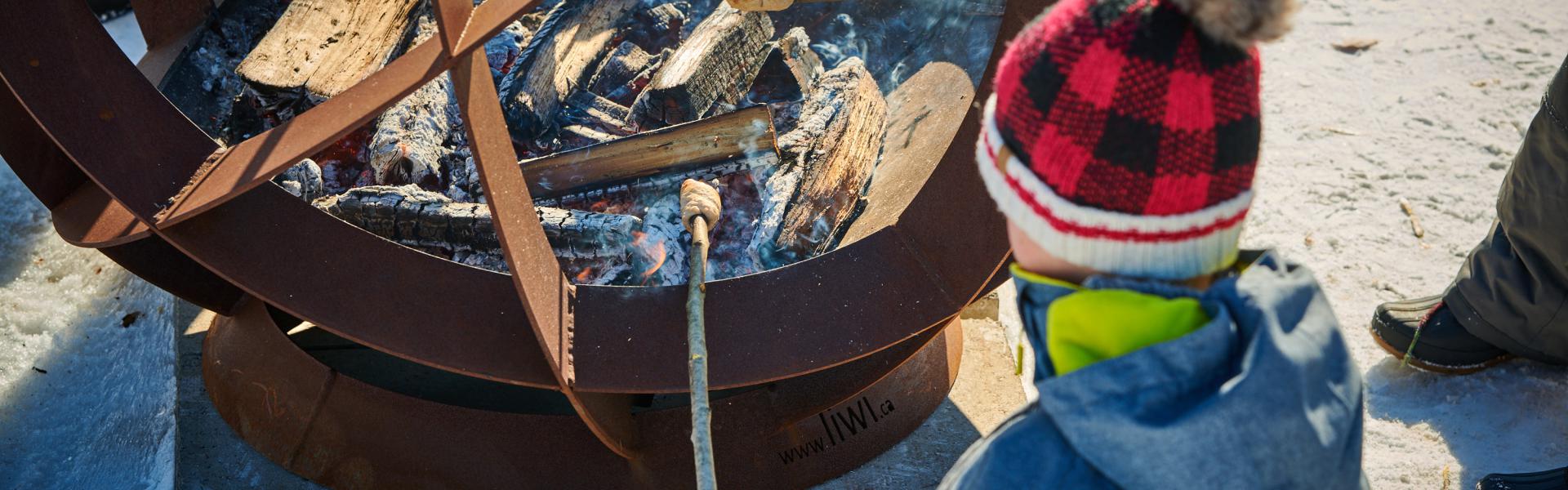 Boy in snow suit roasting bannock over bonfire at an event