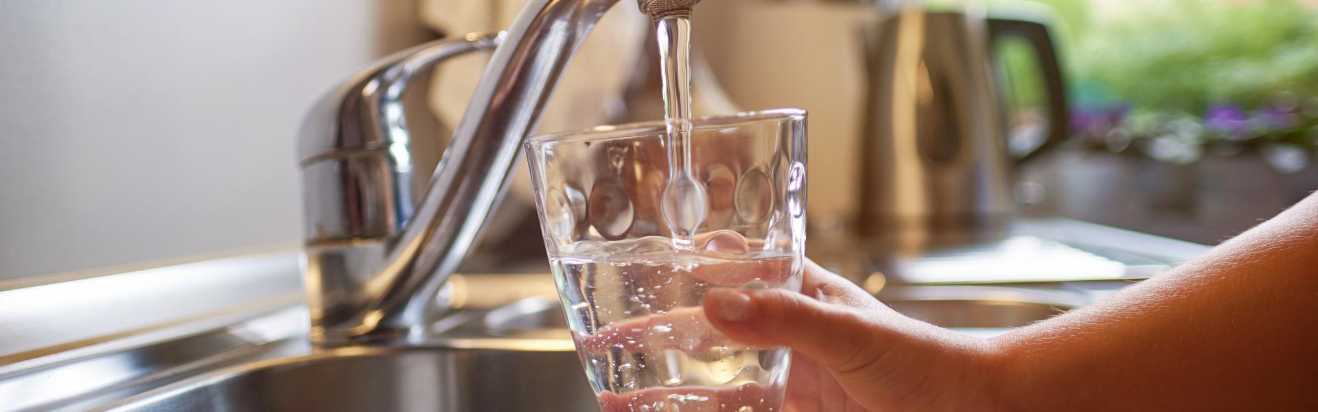 Person filling a glass of water under tap