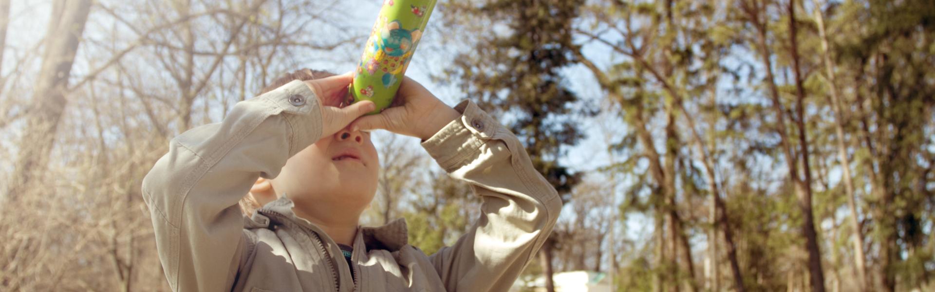 Boy looking through a kaleidoscope outdoors