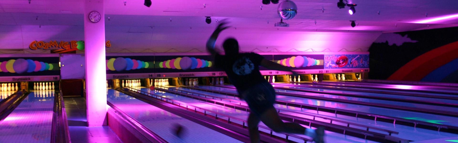 A man bowls a ball down a lane in a cosmic coloured bowling alley