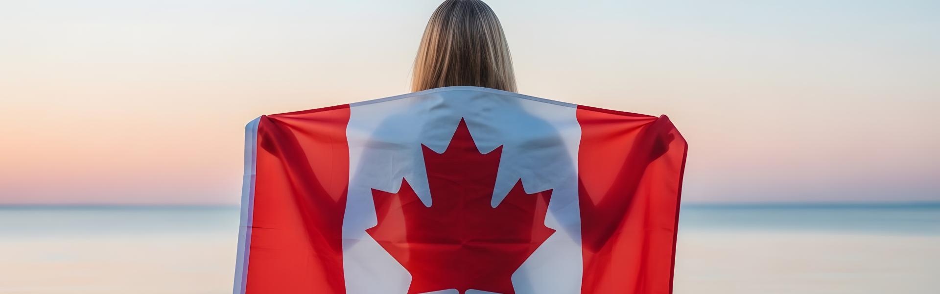 Person standing facing the beach with a canada flag across their back