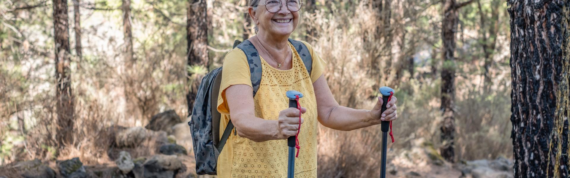A woman in a yellow shirt holding walking poles.