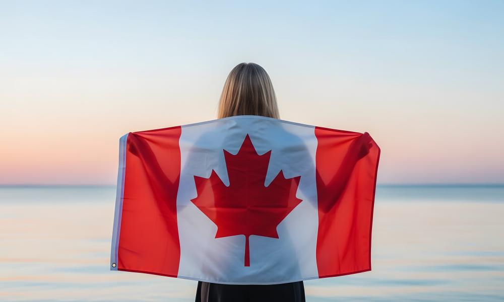 Person standing facing the beach with a canada flag across their back
