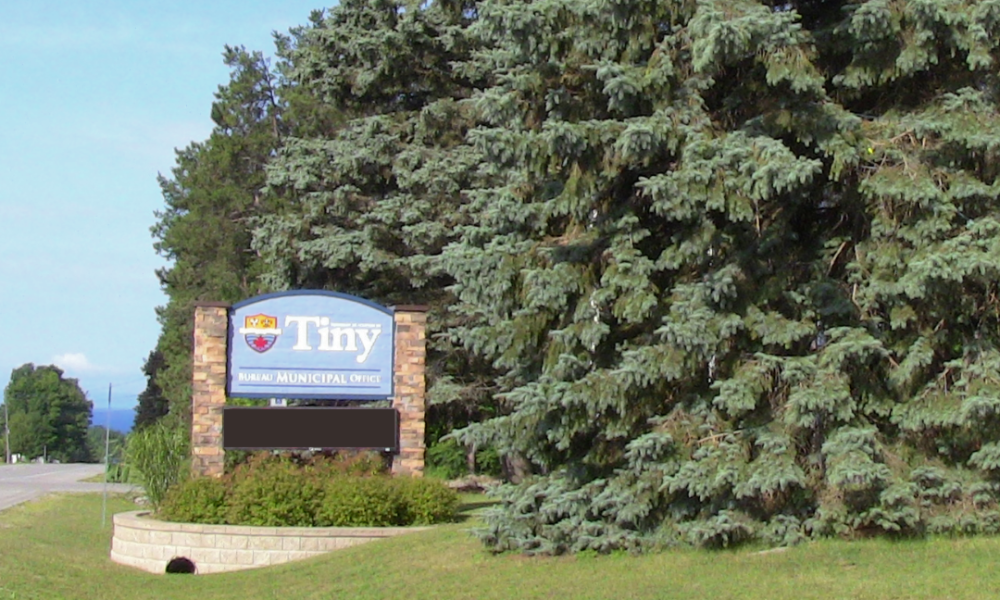 Township of Tiny office sign with large green evergreen trees