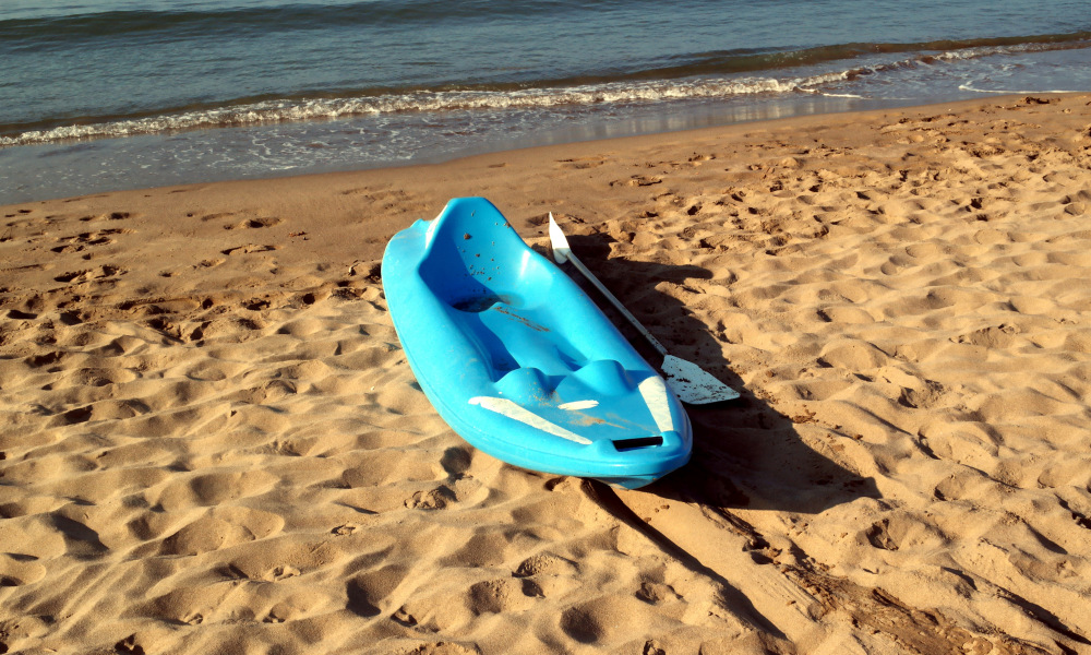 bright blue kayak and paddle sitting on the sand of an empty beach with calm waves coming onto shore