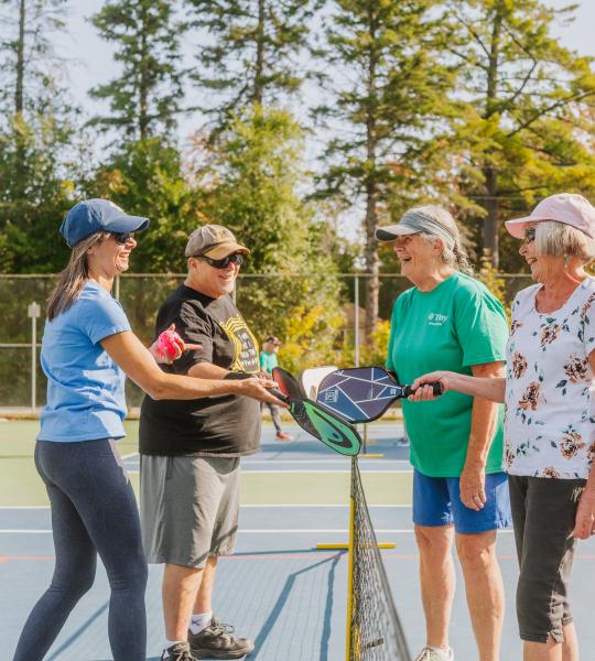 Group playing pickleball gathers at the net after a match to tap paddles
