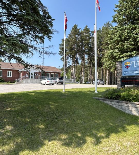 view of the Township of Tiny office from the road featuring the LED Sign, flag poles, and the office building in the background