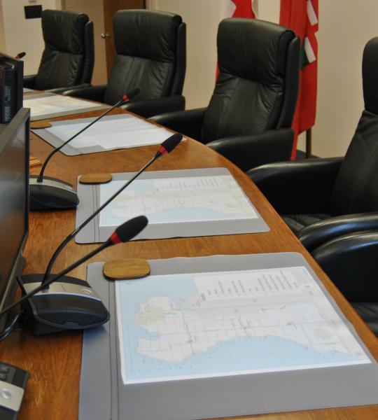 view of the council chambers desk and chairs with maps, microphones, and computer screens on the desk