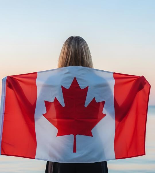 Person standing facing the beach with a canada flag across their back
