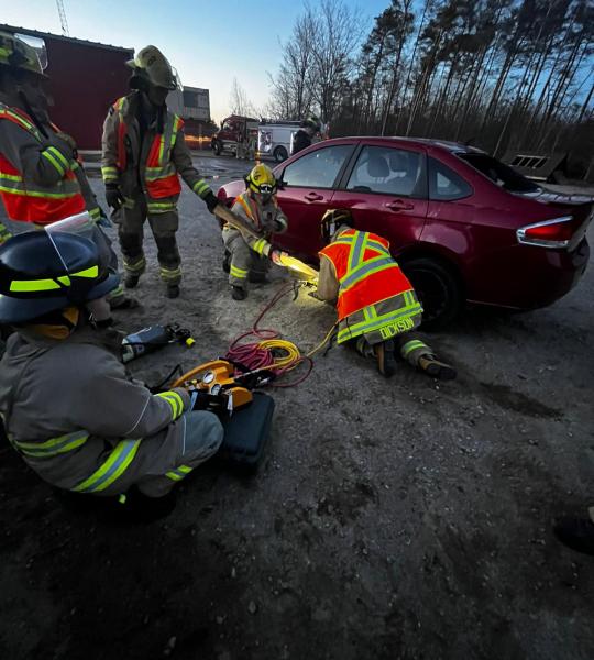 Tiny firefighters training on an older model sedan performing an auto extrication rescue simulation