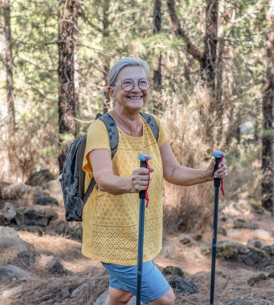 A woman in a yellow shirt holding walking poles.