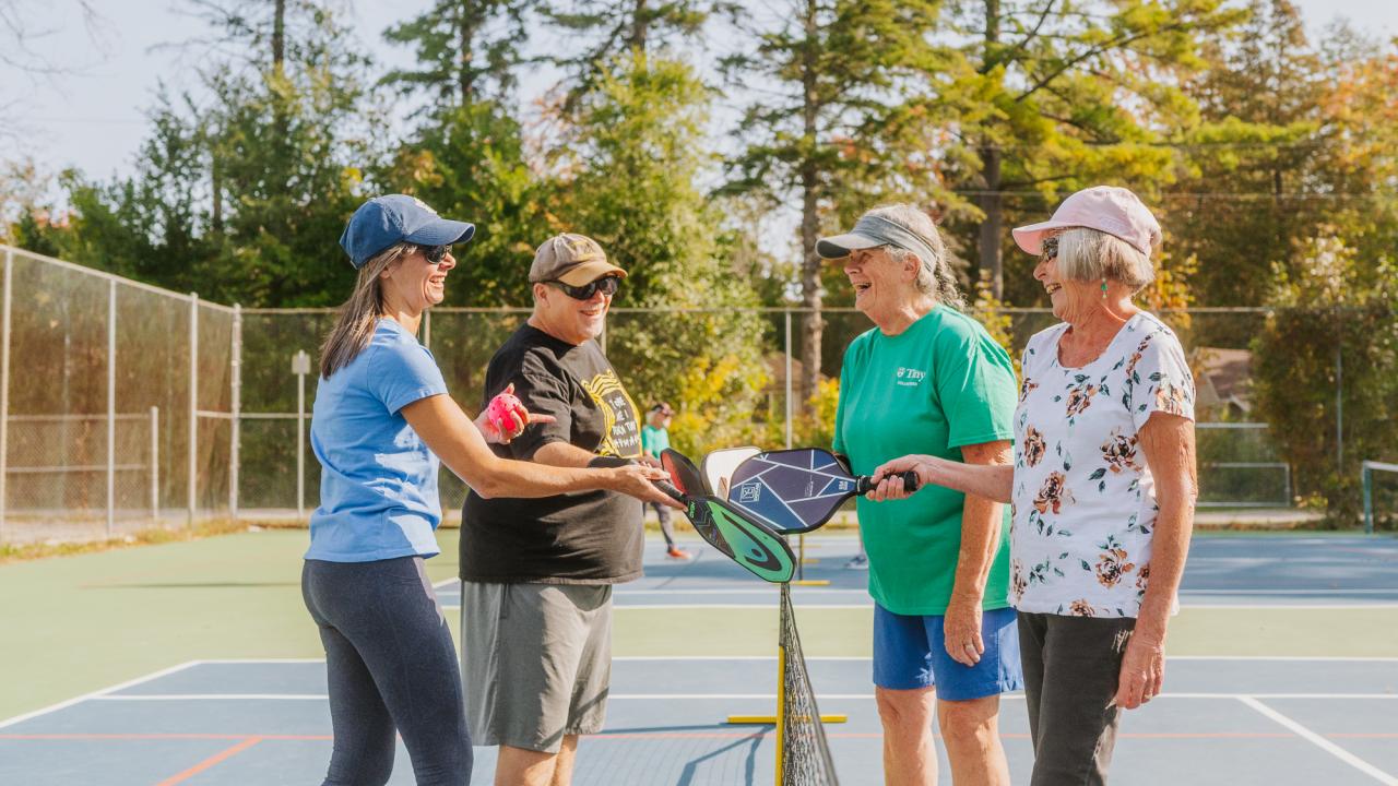 group of four pickleball players tapping paddles over the net at an outdoor court in Tiny on a sunny day