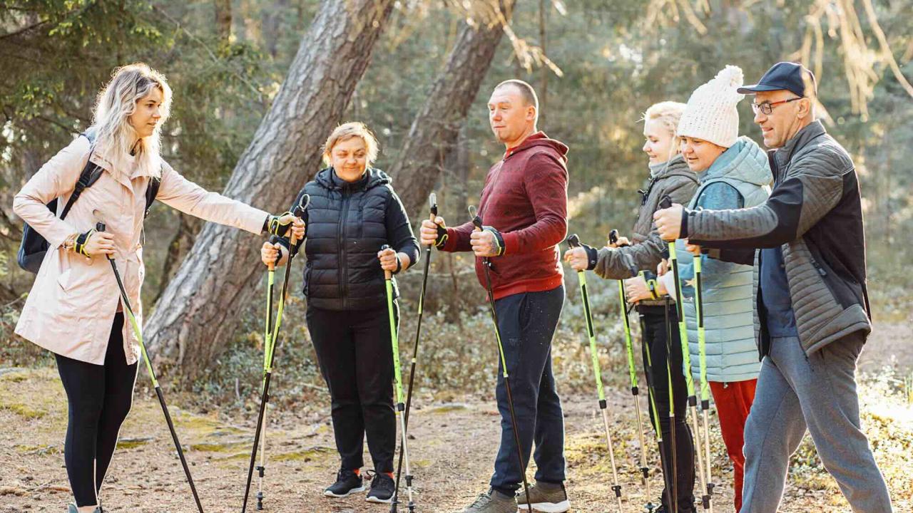 group of older adults receiving a lesson on pole walking from a young woman on a nature trail