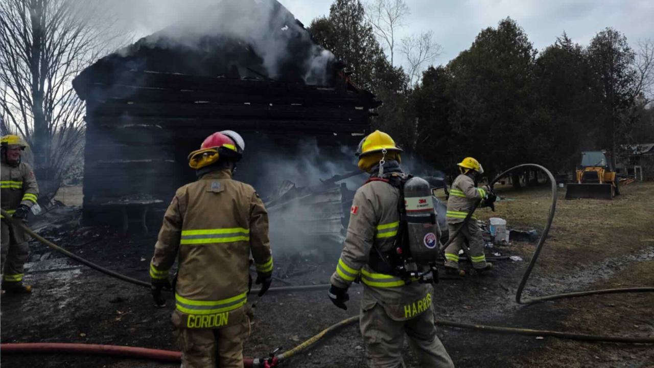 Township of Tiny firefighters at a call with a burnt building in the background with smoke pouring out