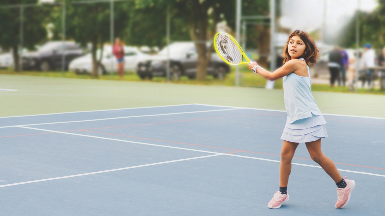 Girl wearing a light blue outfit playing tennis on an ourdoor court in the Township of Tiny during the day