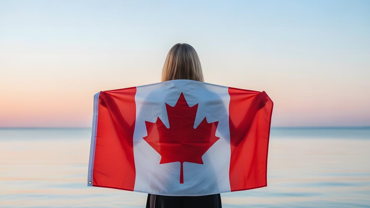 Person standing facing the beach with a canada flag across their back