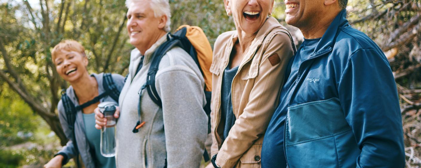 A group of four seniors dressed for fall weather, standing in a row in the forest and laughing.
