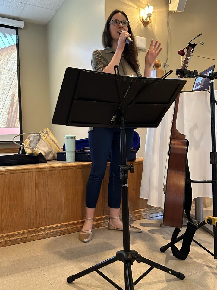 Music therapist speaking to the crowd at the Senior Symposium with a podium for their sheet music and instruments on the side