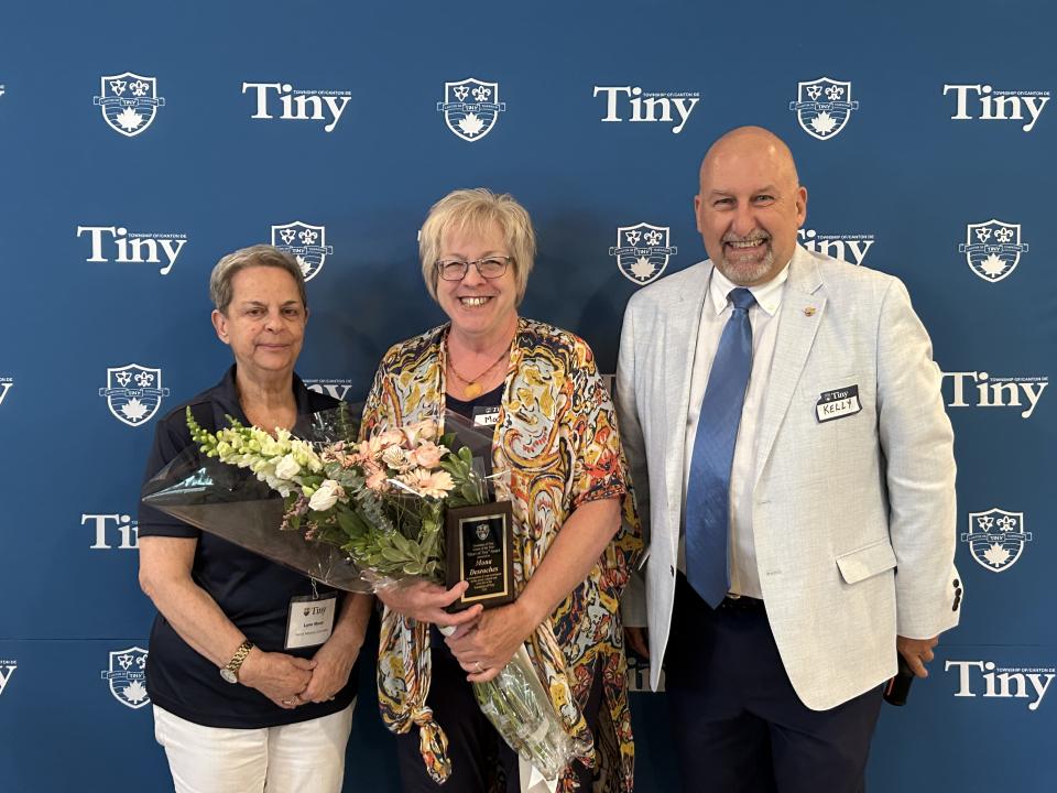 Senior Advisory Committee chair, Senior of the Year award winner Mona Desroches, and Councillor Helowka posing in front of the Tiny photo wall