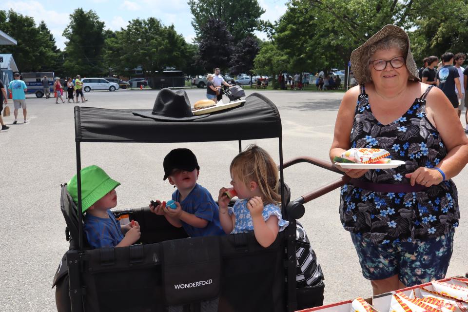 grandmother posing with granchildren in a covered wagon getting lunch for everyone at the bbq table