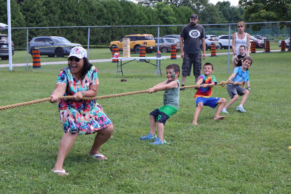 mother with several kids in bright clothing participating in a game of tug of war with other residents watching in the background