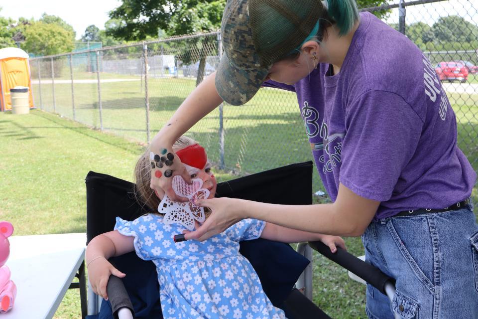 young girl in a blue dress getting their face painted to look like spiderman