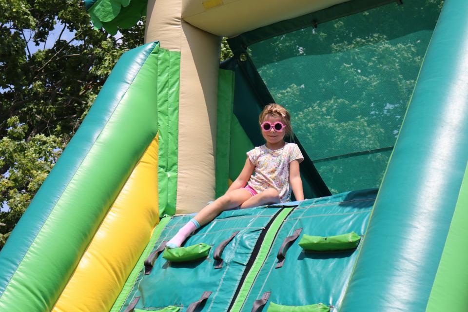 young girl with pink flower shaped sunglasses sitting at the top of the ladder of the inflatable