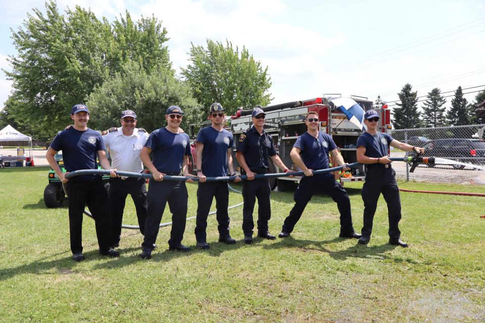 group of 7 volunteer firefighters posing and laughing, all holding the fire hose with water running