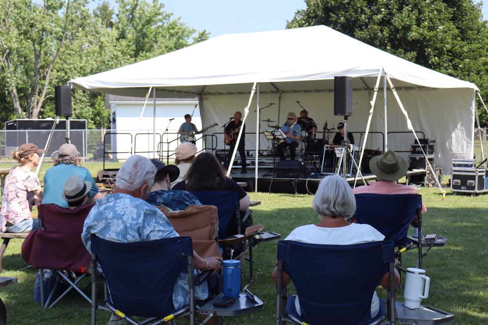 crowd sitting on lawnchairs in the shade enjoying live music under the tent