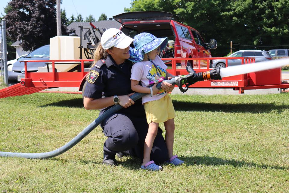female firefighter in uniform helping a child spray water from a fire hose