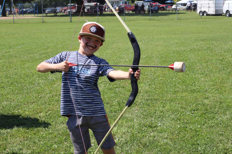 boy with moustache facepaint posing with the bow and arrow at the archery booth in the rec zone