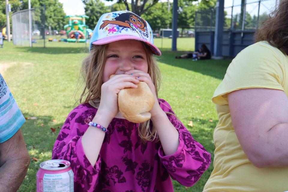 girl in a bright pink shirt and hat taking a bite out of their hotdog 