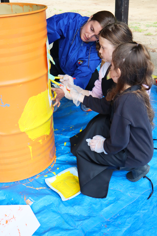 staff helping young students paint a waste barrel