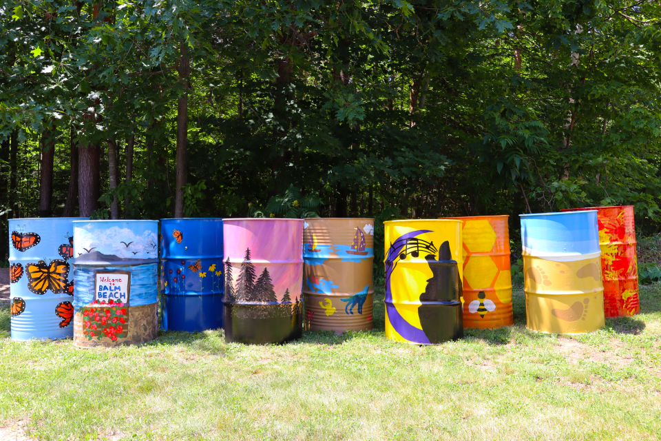 nine staggered colourfully painted barrels following themes of Tiny's natural environment, beaches, french heritage, and pollinators