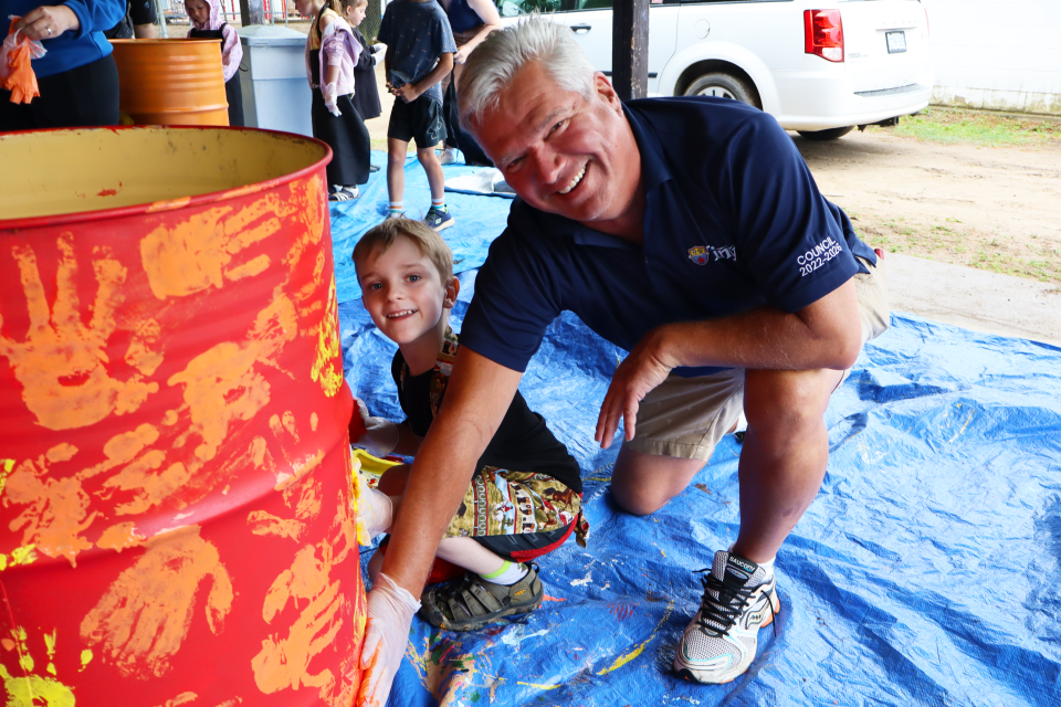 Mayor David Evans and a young student putting handprints on a bright red waste barrel