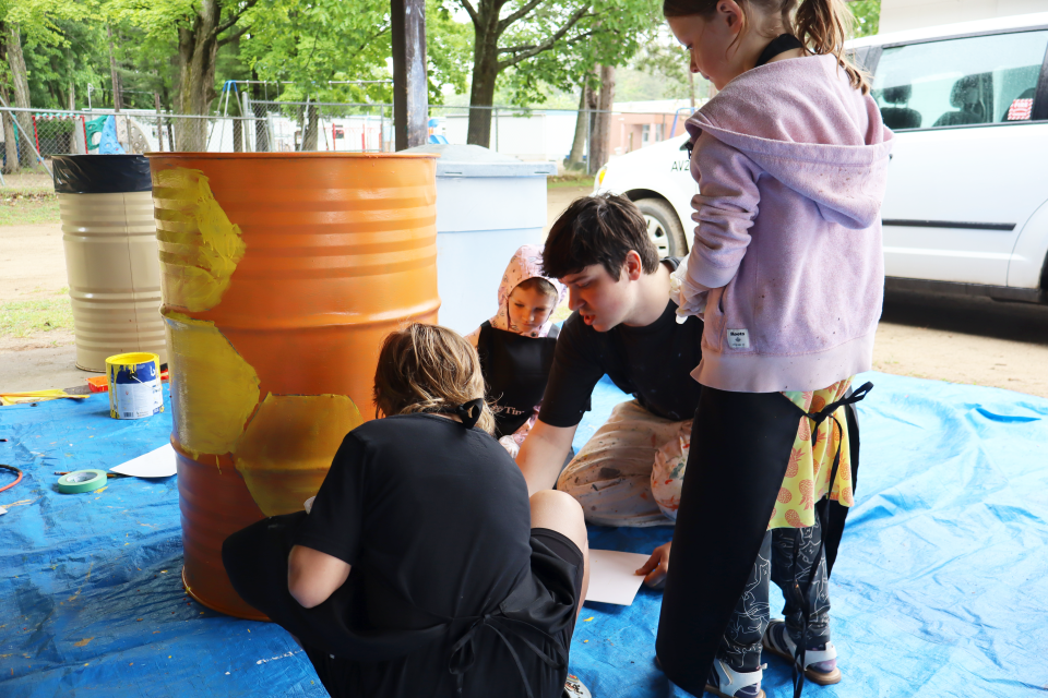 local artist with several students painting a bright orange waste barrel