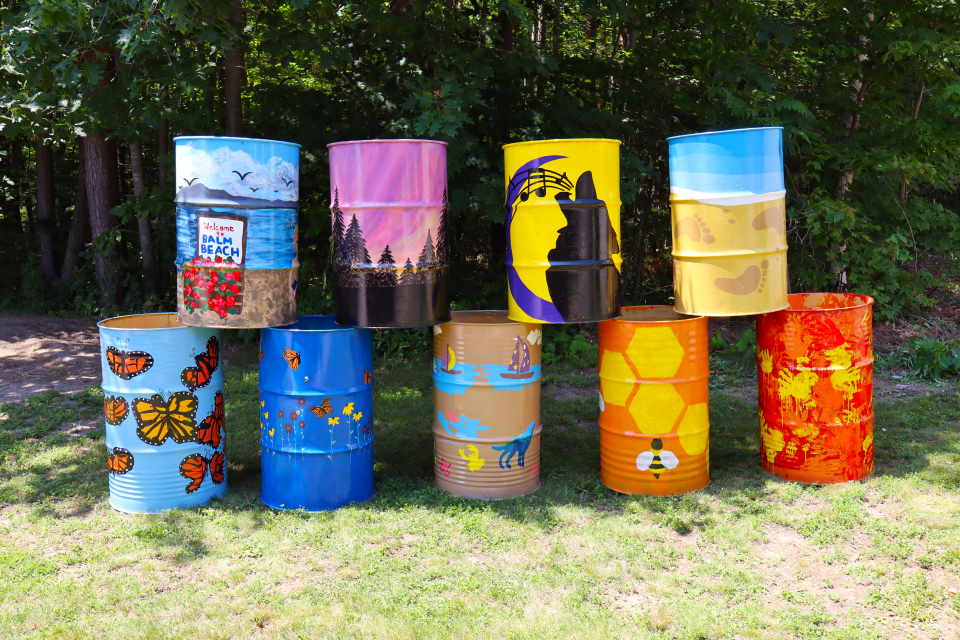 group of nine colourfully painted barrels with four stacked on five below, each with a slightly different theme ranging from Tiny's beaches, french heritage, the environment, and pollinators