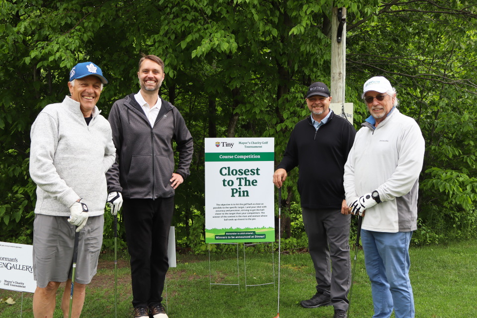 Golf foursome posing together at the Closest to the Pin hole sign.