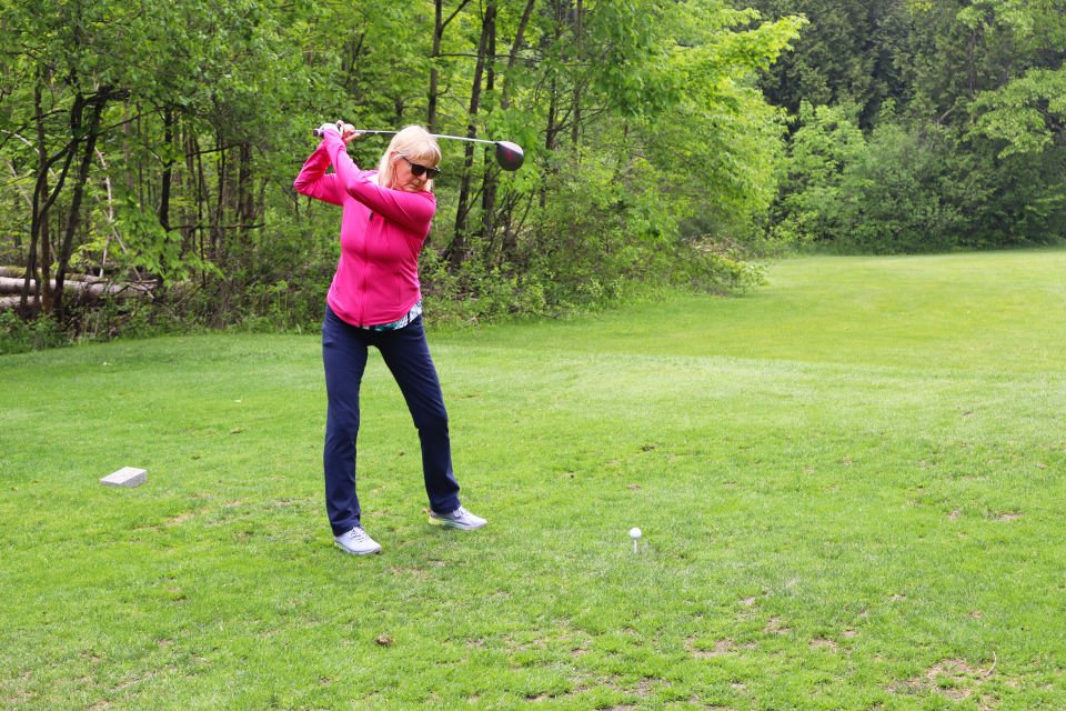Woman in a bright pink sweater lining up their golf swing.