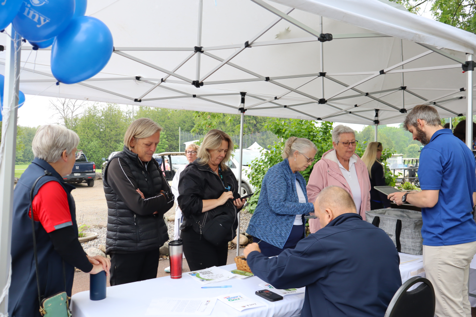 staff and councillor Helowka helping golf participants sign in under a tent with branded tiny balloons
