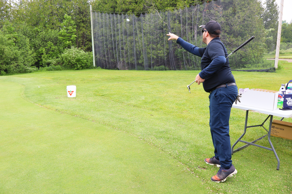 Man participating in a course game mid-throw of a golfball toward a branded Canadian Tire bucket on the grass.