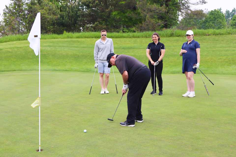 Man mid-putt toward the pin with their golf team standing behind them watching.