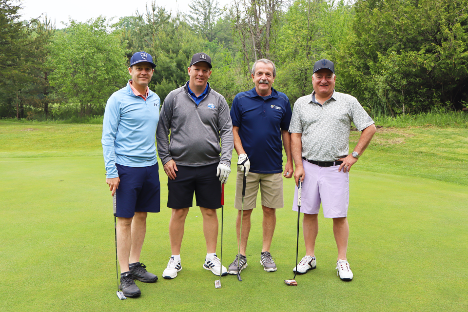 Golf foursome out on the greens posing together with their golf clubs.