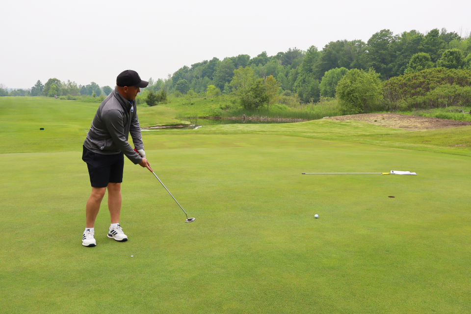 Man mid-putt watching the golf ball roll toward the hole, with the white flag laying on the ground.