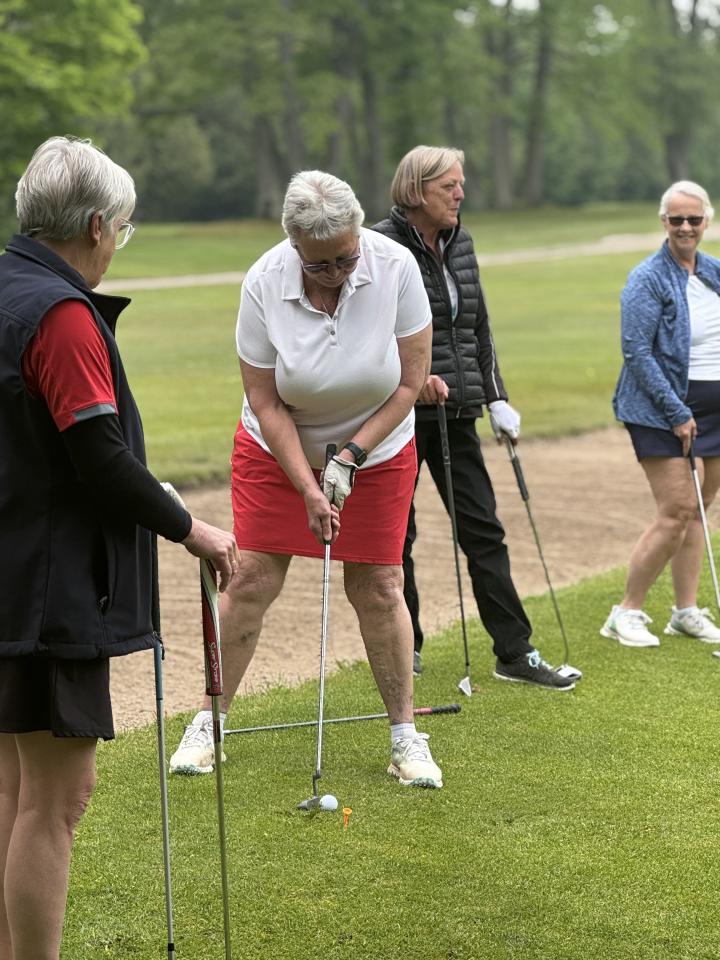 All woman golf foursome standing close by while one lines up a putting shot.