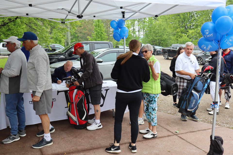 Golf participants signing in at the registration table under a tent with bright blue Tiny balloons.