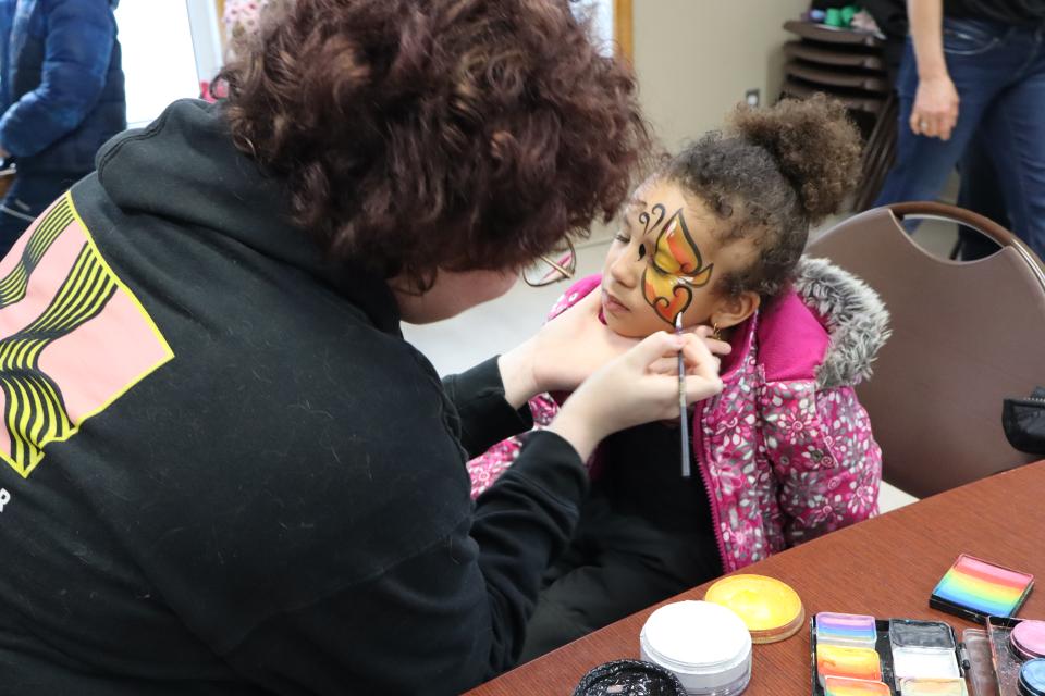Face paint artist actively painting a butterfly on a young girl's face