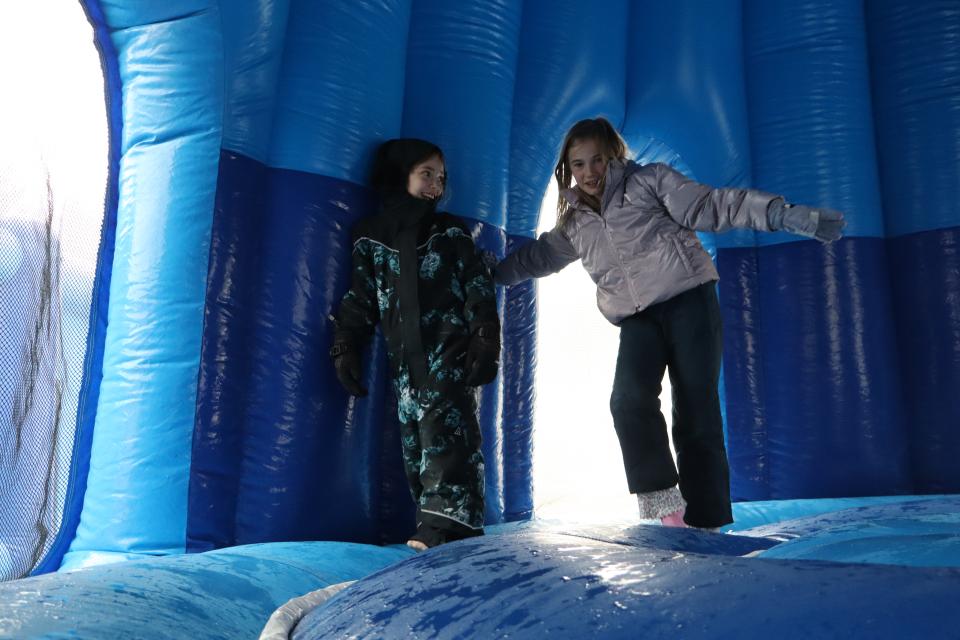 Two girls dressed in winter gear inside the snowman bouncy castle lined with bright blue walls and light shining inside