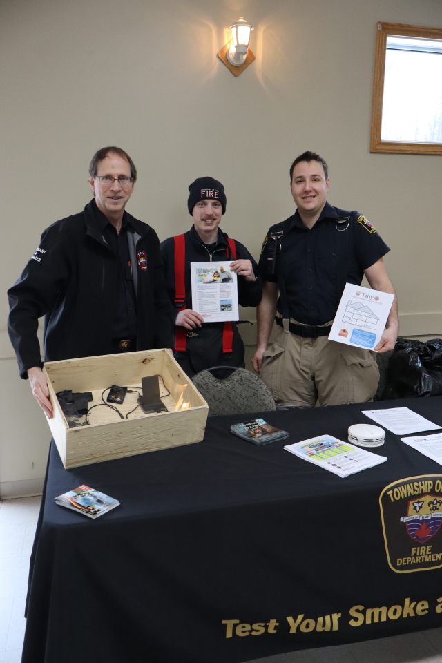 Members of Tiny Fire showing off their booth items, including a burnt phone and lithium ion battery in a shadow box