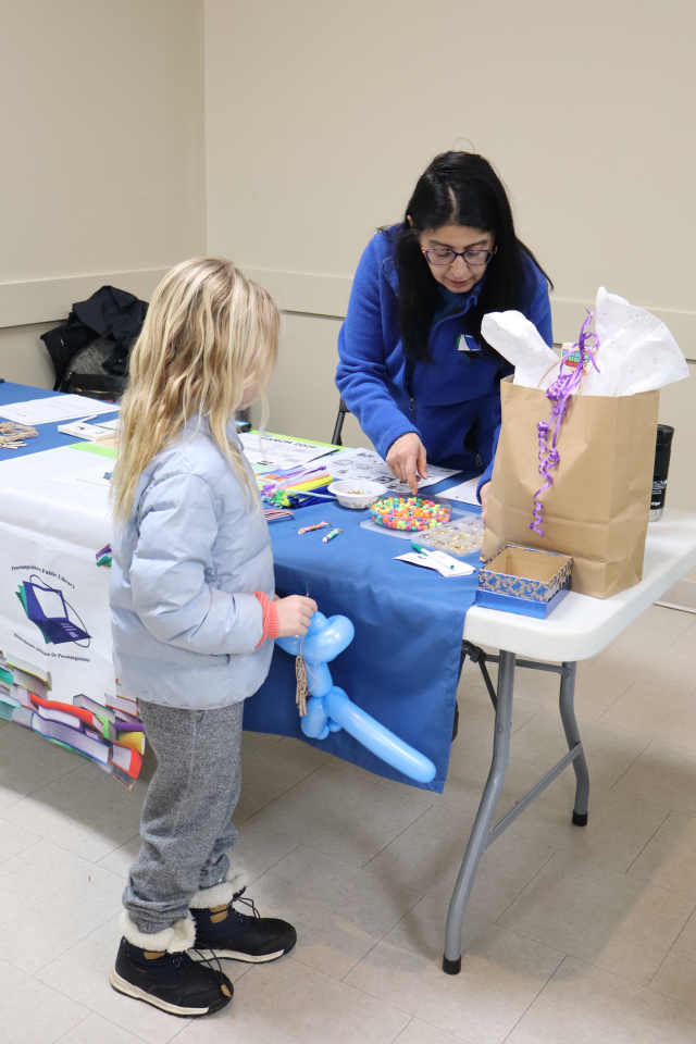 Girl at the Penetanguishene Public Library booth talking to staff about the bead craft